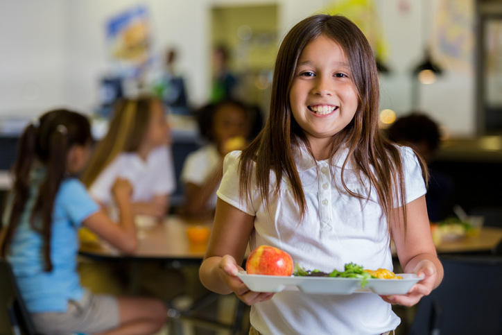 Happy elementary school girl with healthy food in cafeteria